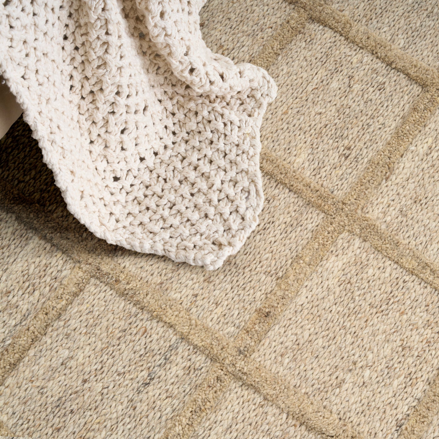 Beige geometric rug with square pattern and a cream chunky knit blanket draped over it.