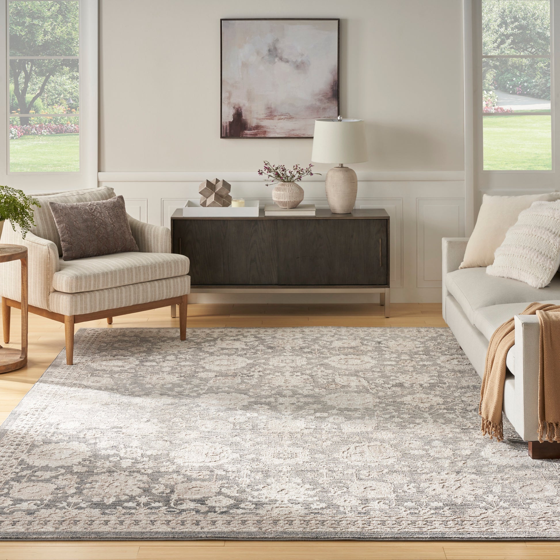 Neutral living room with beige armchair, gray sofa, a patterned rug (6' x 9'), dark wood sideboard, abstract art & lamp.