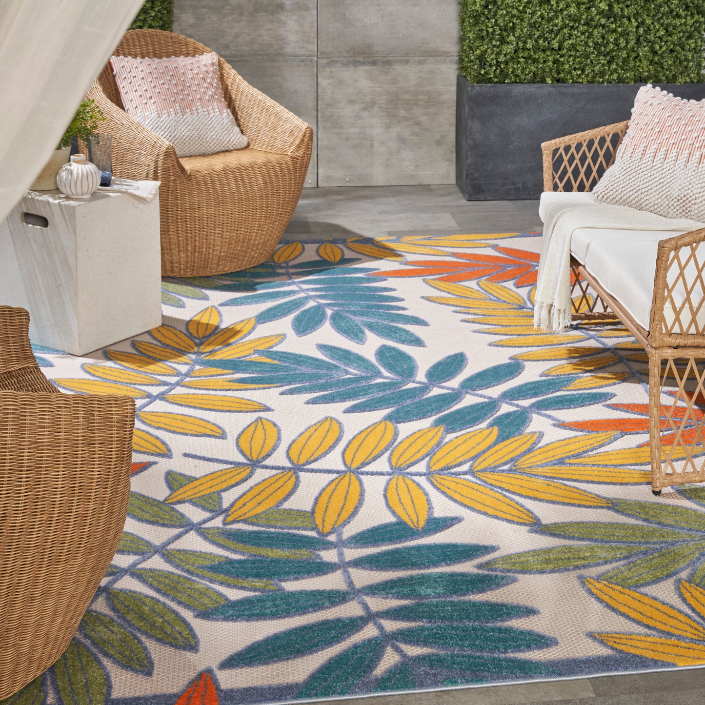 Outdoor patio with a colorful yellow and teal leaf-pattern rug; wicker chairs with white cushions.