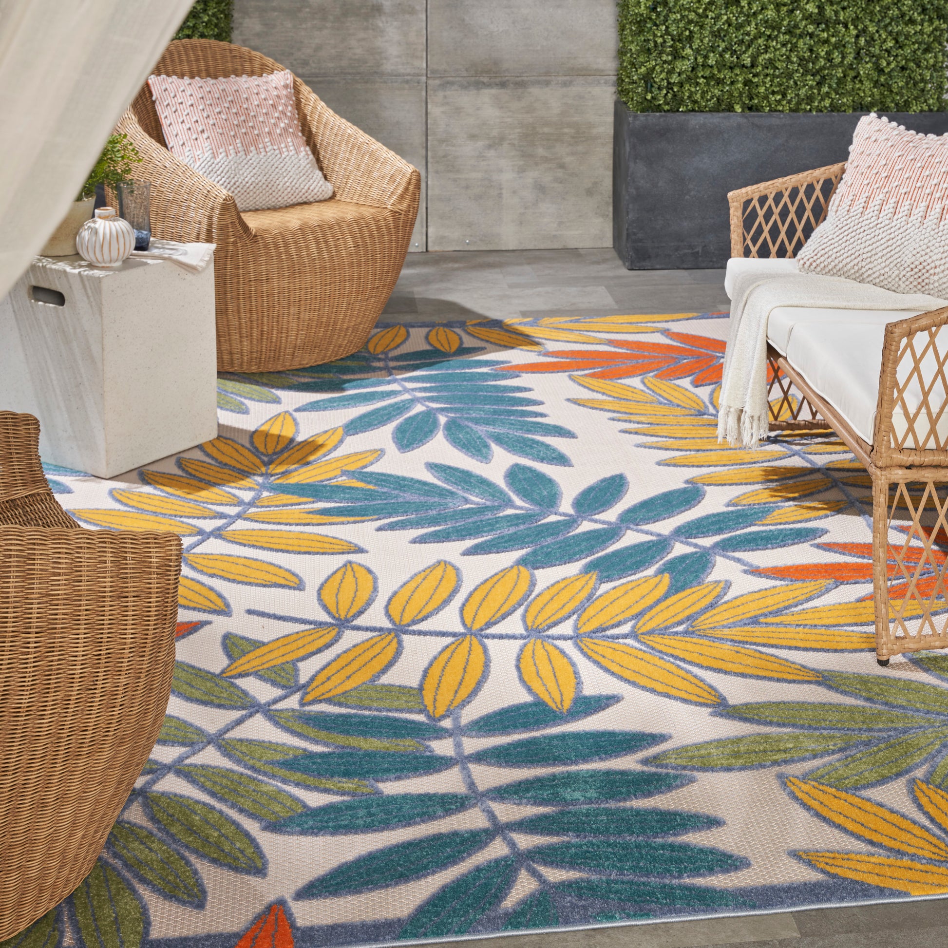 Outdoor patio with a colorful yellow and teal leaf-pattern rug; wicker chairs with white cushions.
