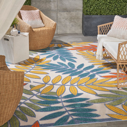 Outdoor patio with a colorful yellow and teal leaf-pattern rug; wicker chairs with white cushions.