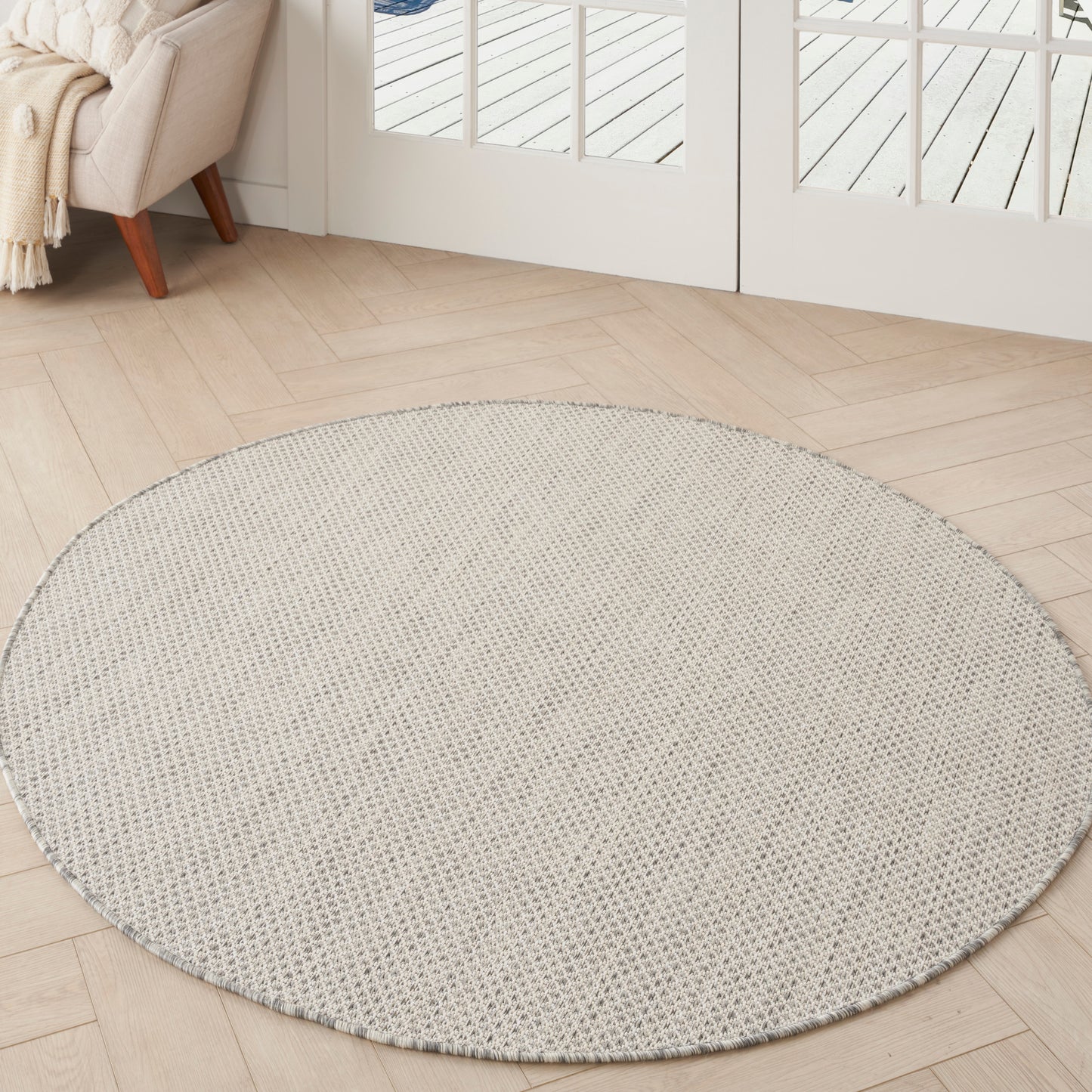 Round beige woven area rug on light wood floor in bright living room with cream sofa and throw near glass doors.