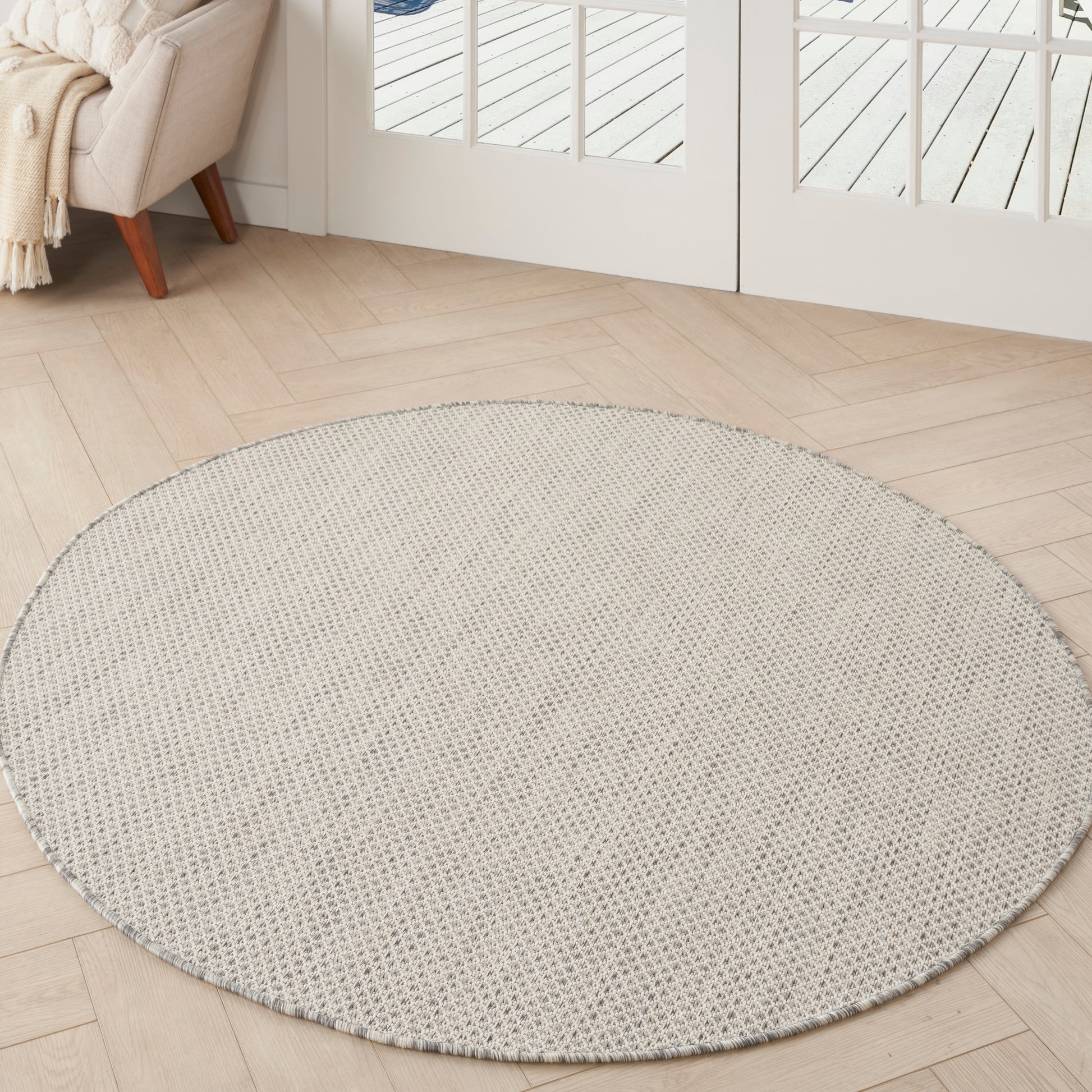 Round beige woven area rug on light wood floor in bright living room with cream sofa and throw near glass doors.