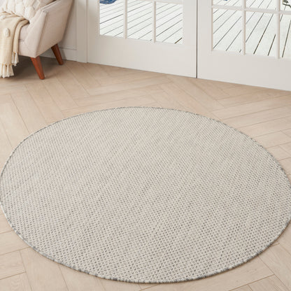 Round beige woven area rug on light wood floor in bright living room with cream sofa and throw near glass doors.