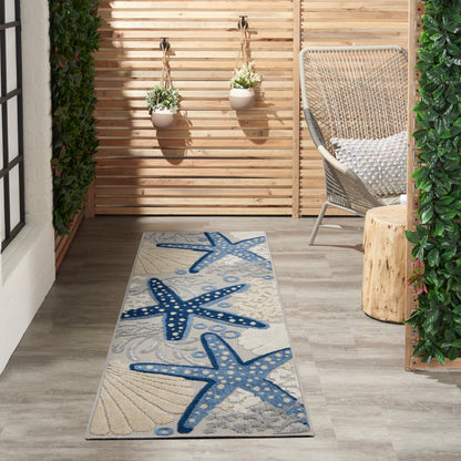 Outdoor runner rug featuring blue starfish pattern on beige background, laid on wooden deck beside wicker chair and planters.