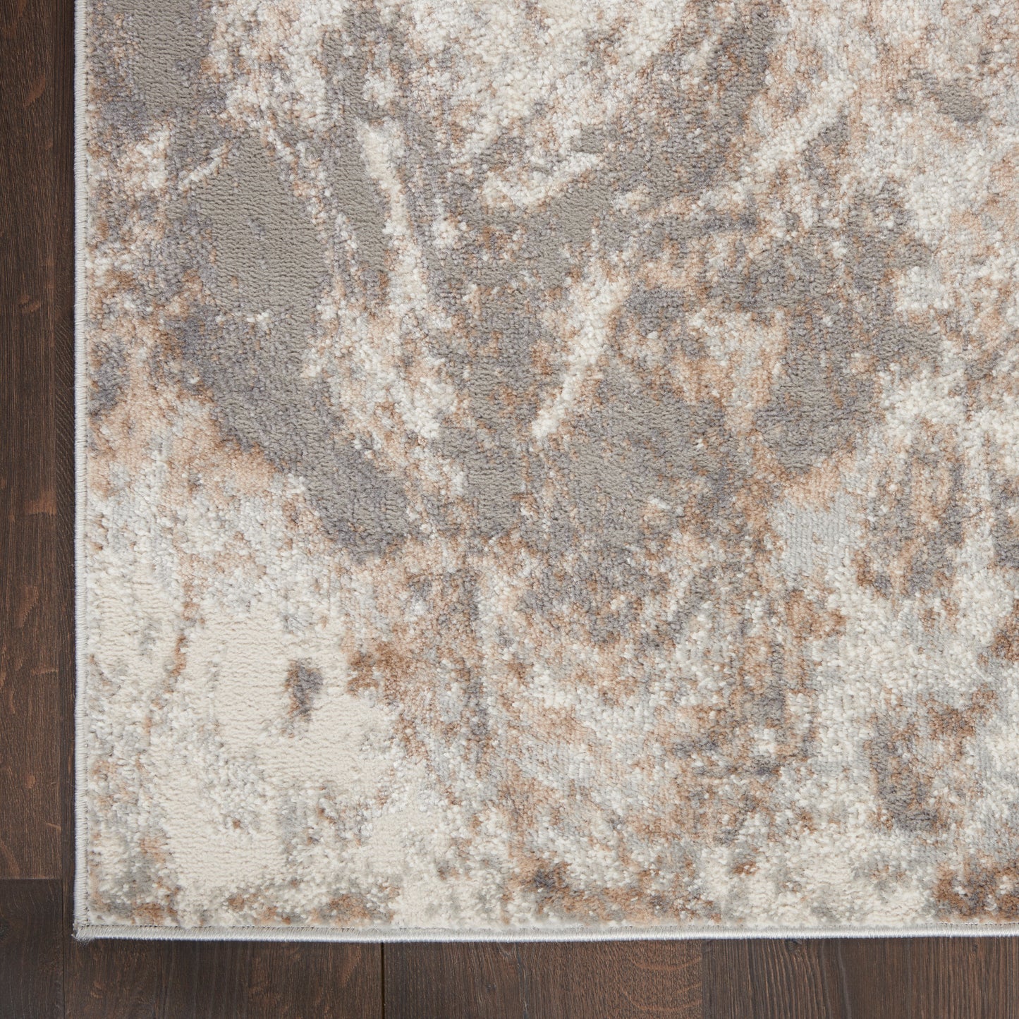 Abstract beige, gray and brown area rug with a distressed pattern on a dark wood floor; light border along edge.