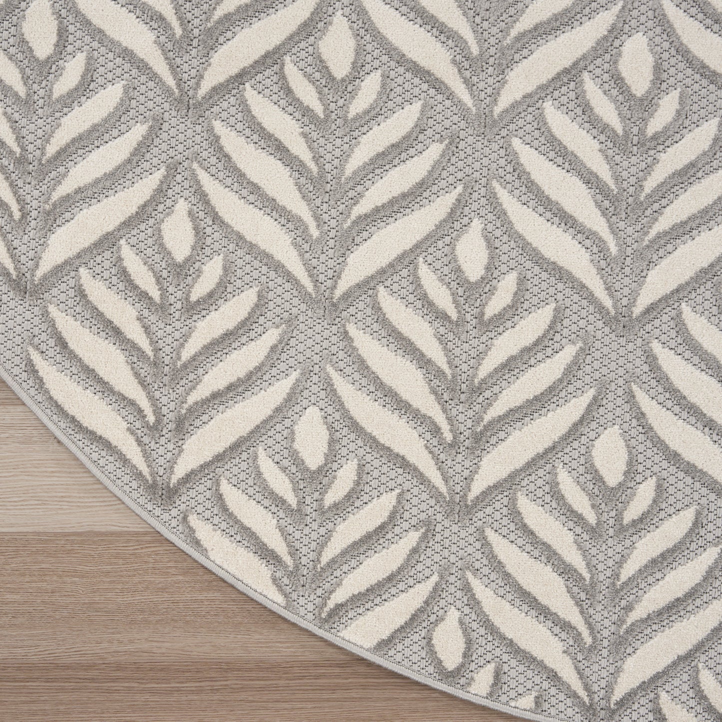 Circular gray and cream tropical leaf-pattern rug with woven texture on a wooden floor.