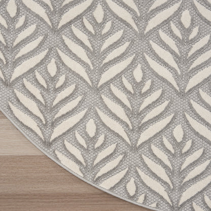 Circular gray and cream tropical leaf-pattern rug with woven texture on a wooden floor.
