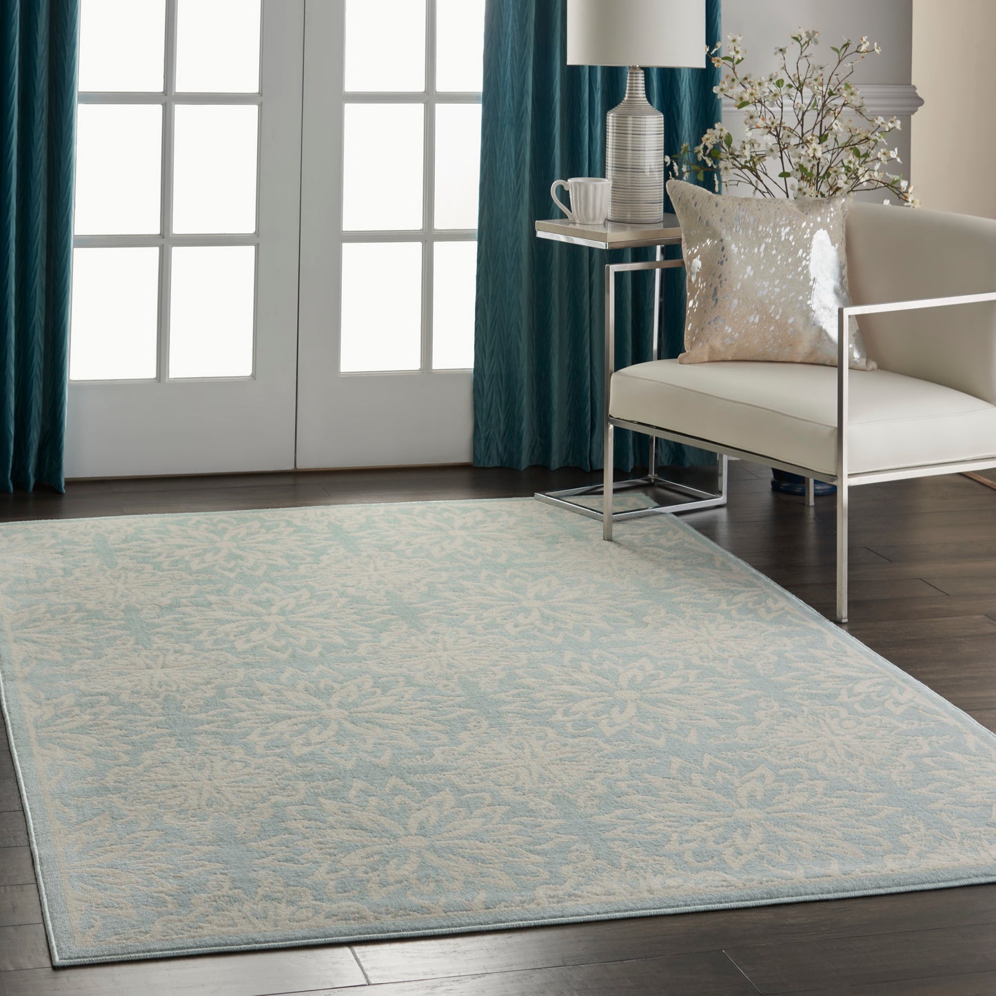 Light blue patterned area rug with cream floral motif in a modern living room with a white armchair and teal drapes.