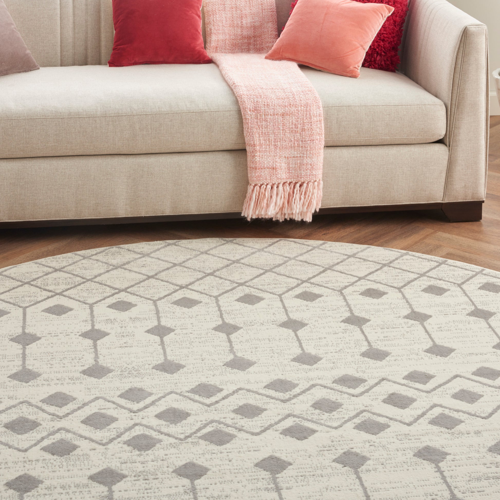 Beige round rug with a light gray geometric pattern on a wooden floor.