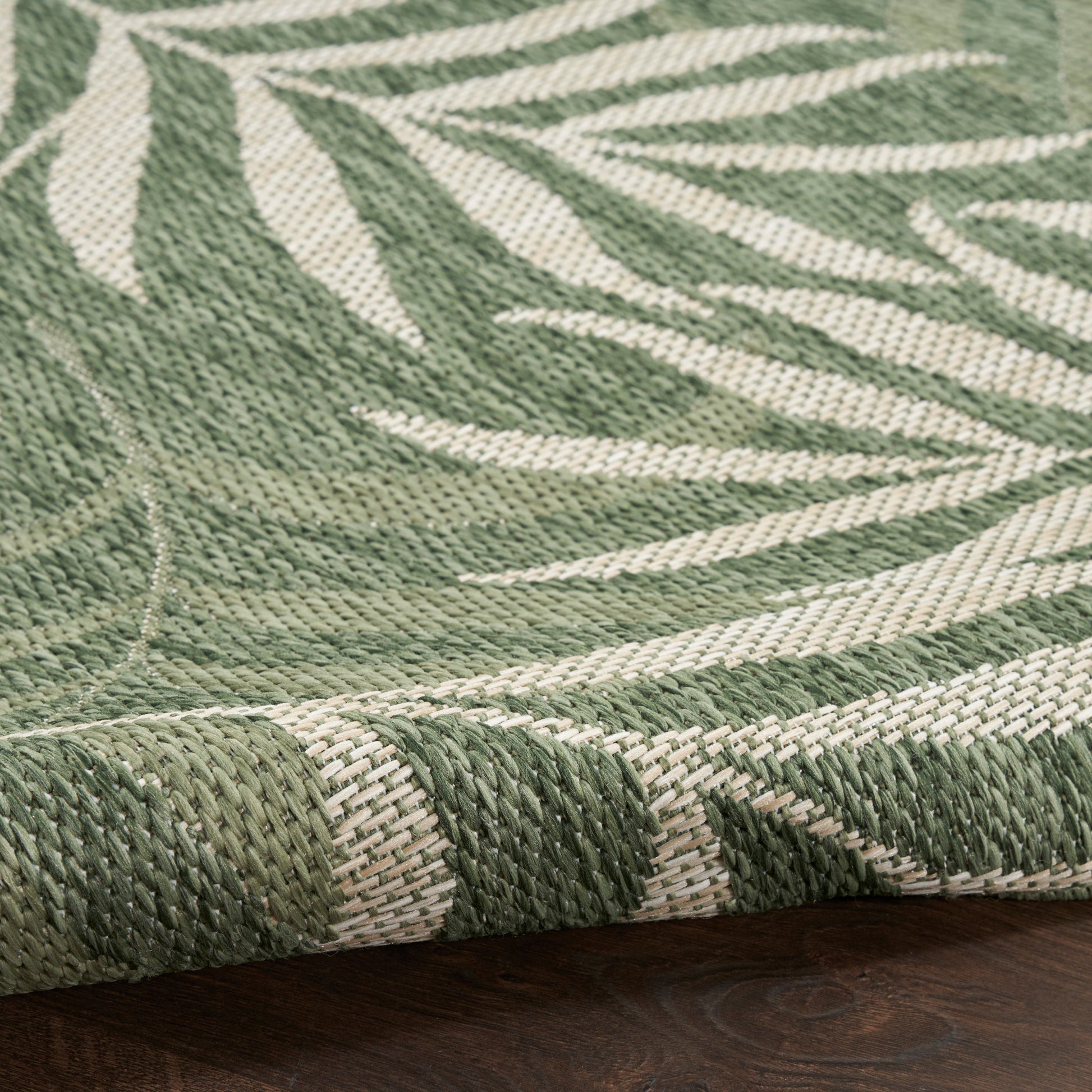 Close-up of green & cream woven runner rug with botanical leaf pattern, rolled edge, on dark wood floor.