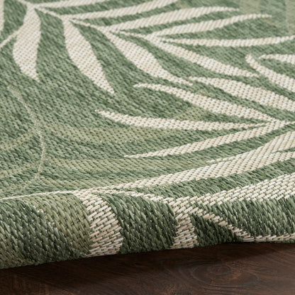 Close-up of green & cream woven runner rug with botanical leaf pattern, rolled edge, on dark wood floor.