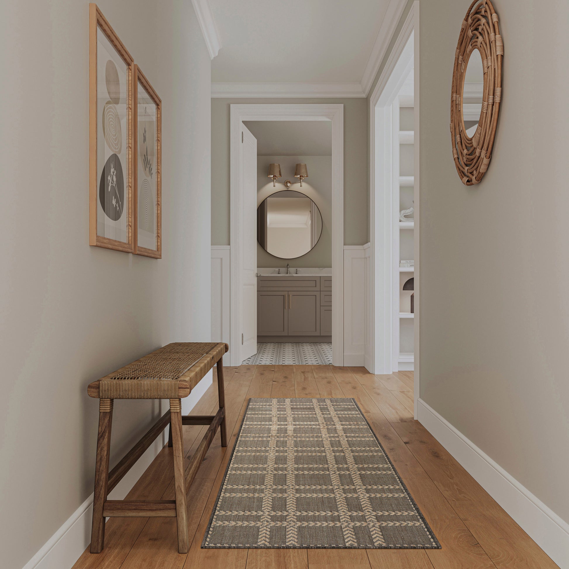 Neutral hallway with wooden bench, geometric woven rug, framed art, round wicker mirror, leads to the bathroom.