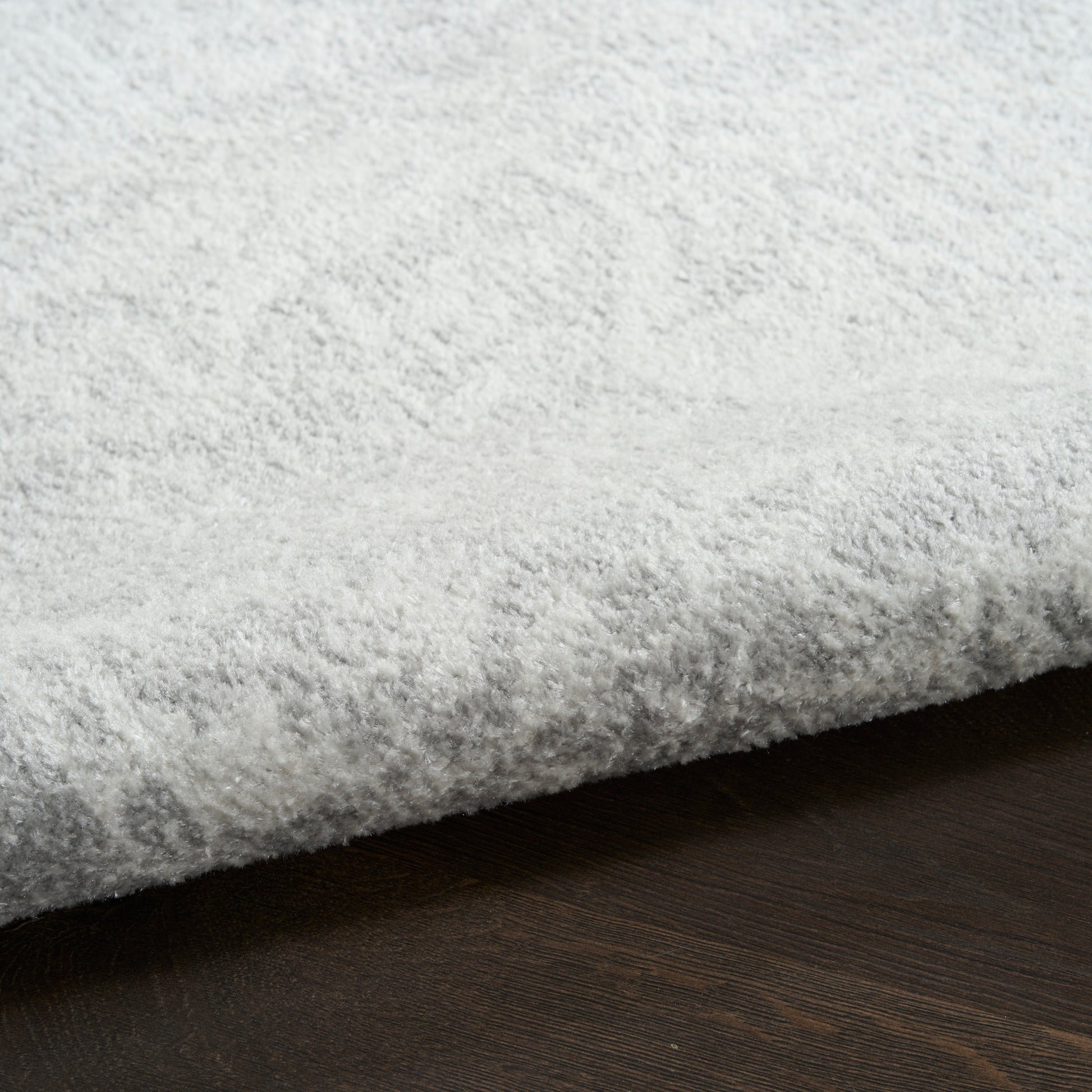 Plush light gray shag rug with high pile on dark wood floor, cozy living room decor.