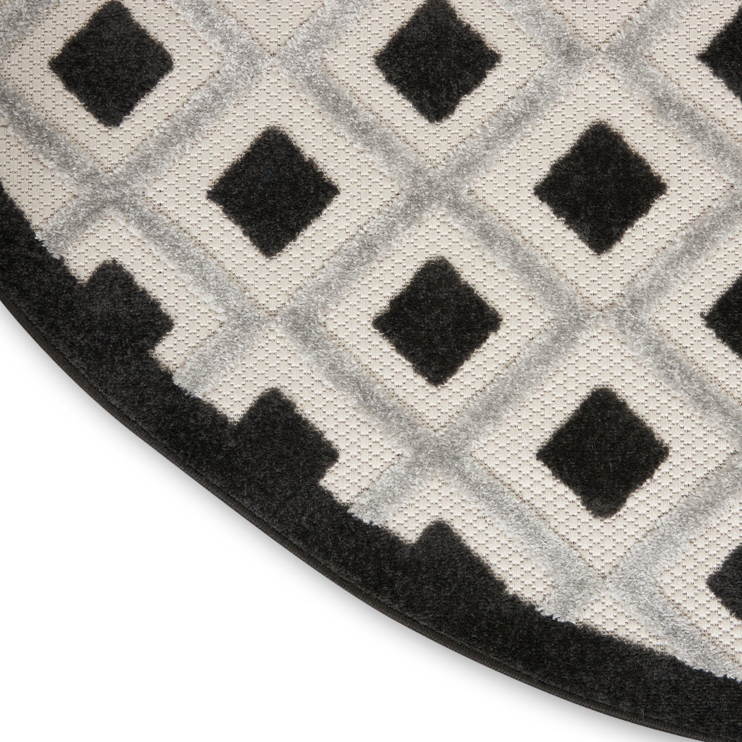 Close-up of a circular rug with light gray and black diamond lattice, plush pile, and a black stair-step border.