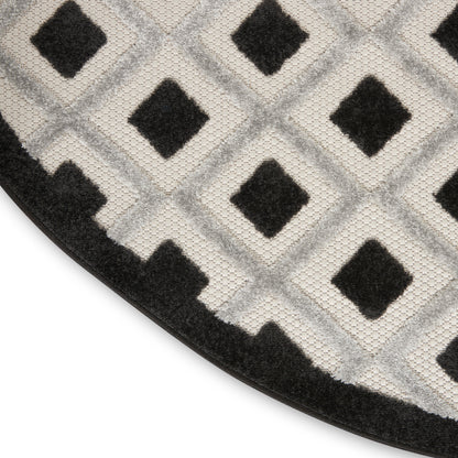 Close-up of a circular rug with light gray and black diamond lattice, plush pile, and a black stair-step border.