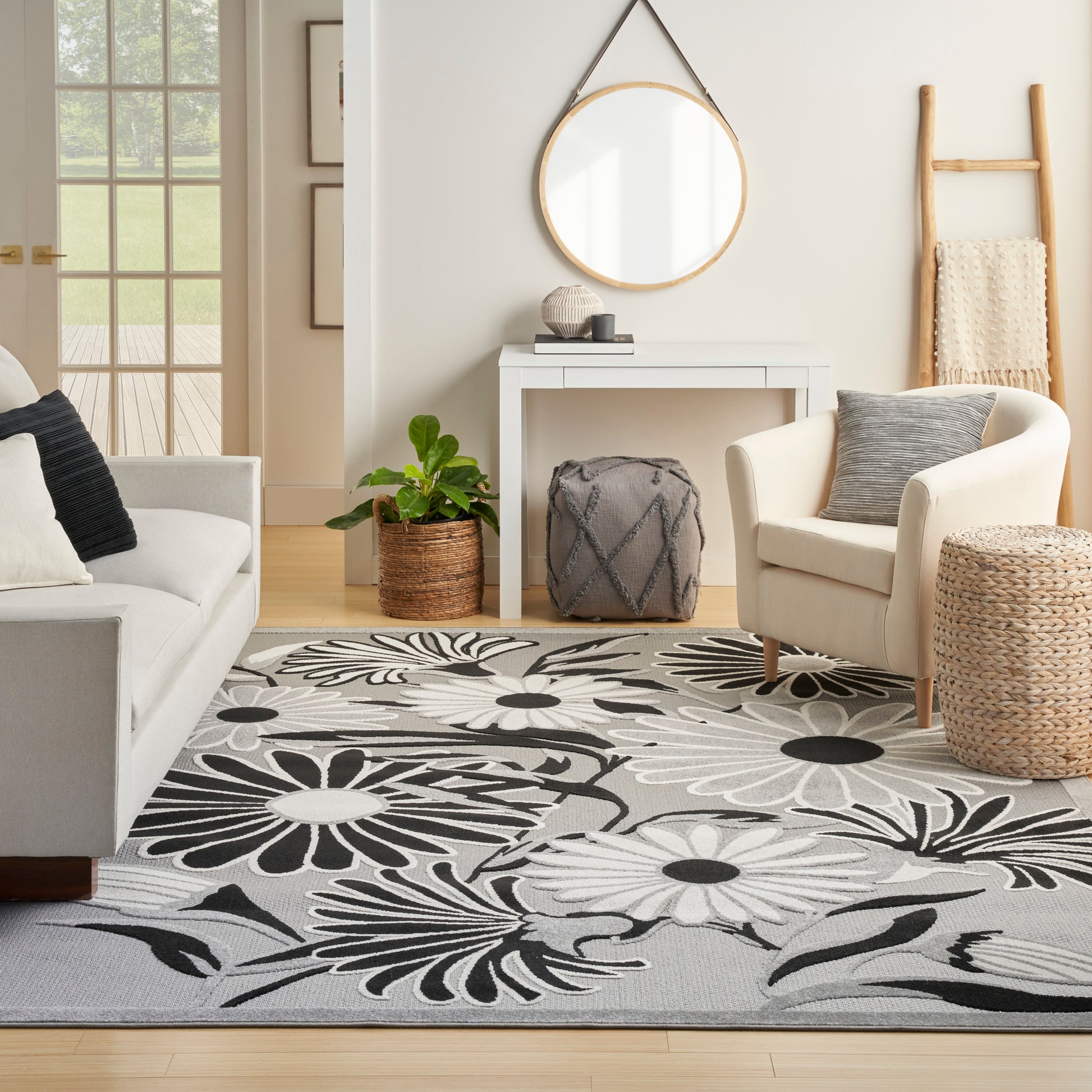 Cozy living room with a large gray floral rug, cream sofa and armchair, round mirror, and natural wicker accents.