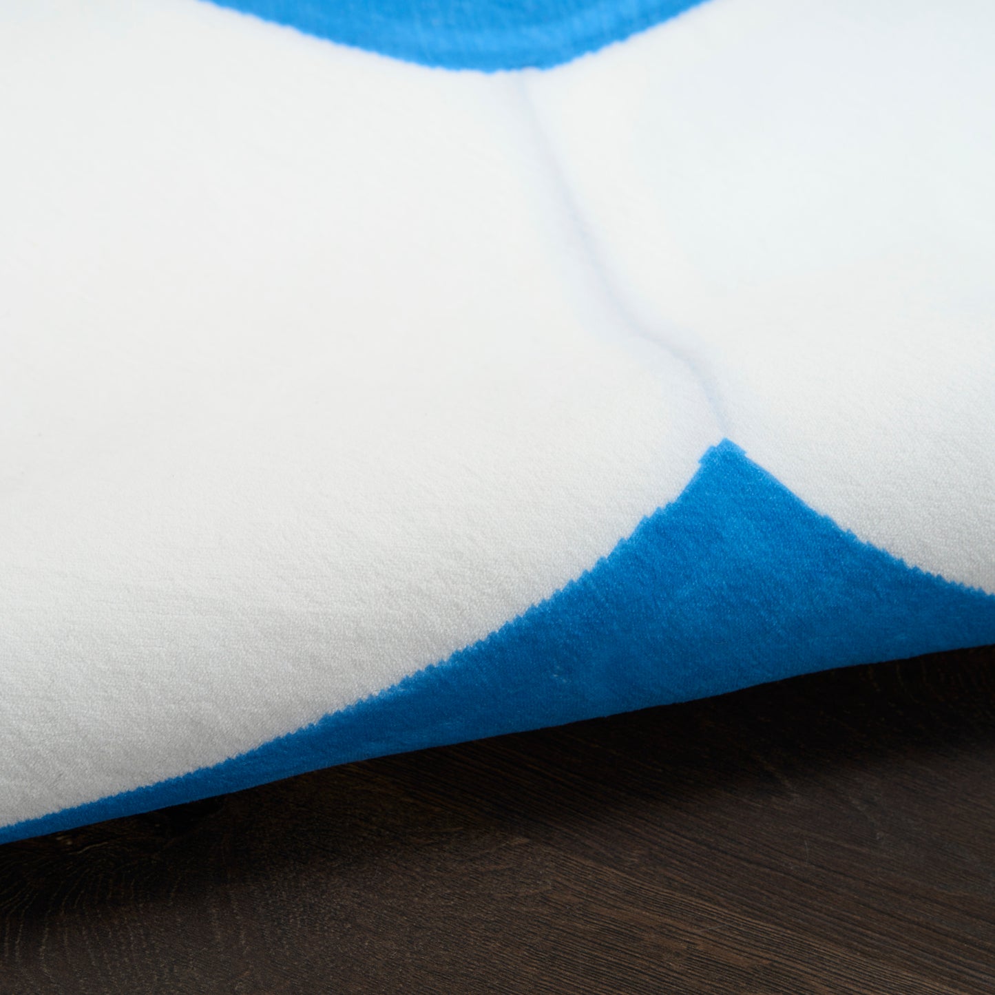 Close-up of white and blue plush rug with bold blue triangles on a dark wooden floor.