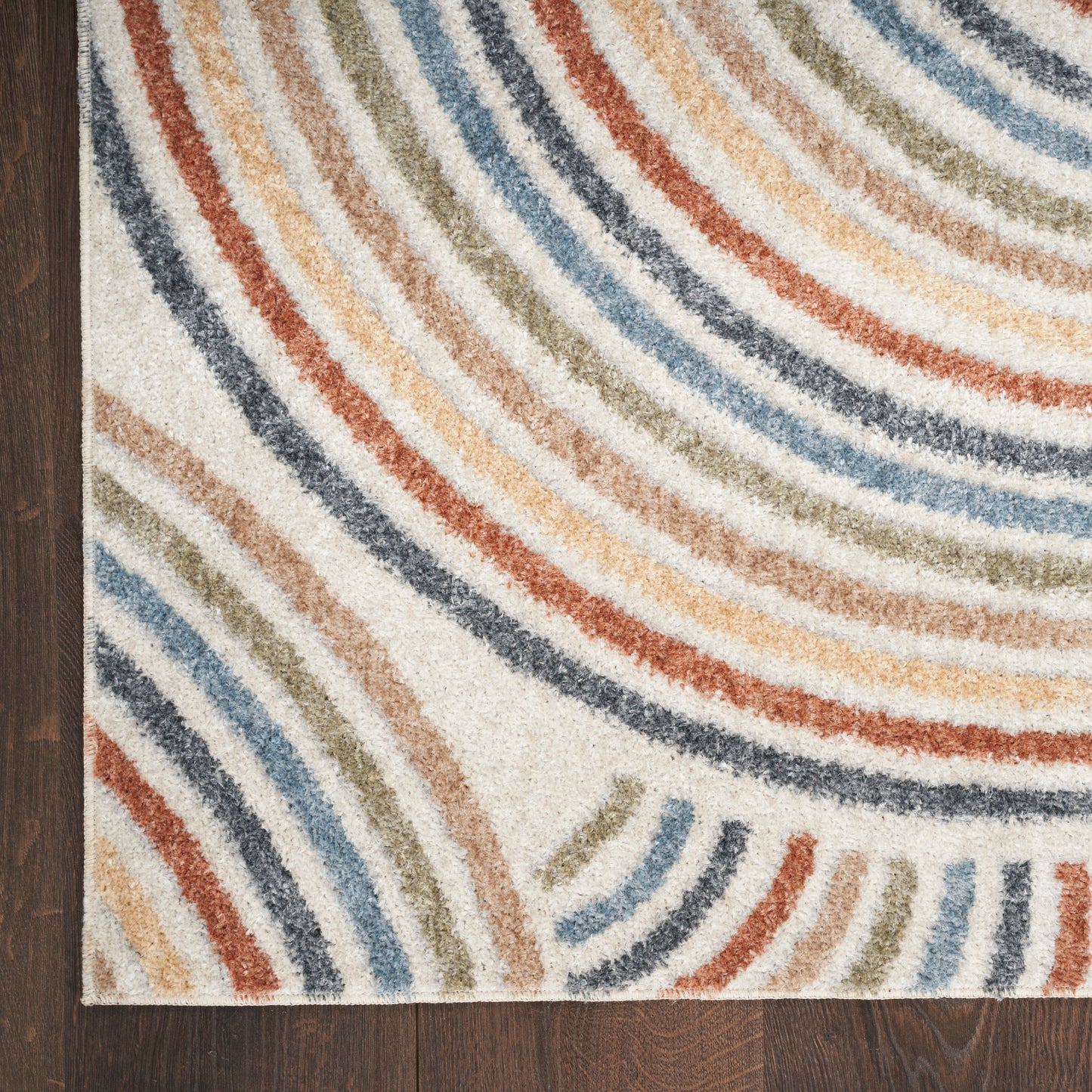 Multicolor curved striped area rug with blues, oranges and beiges on white, laid on dark wood floor