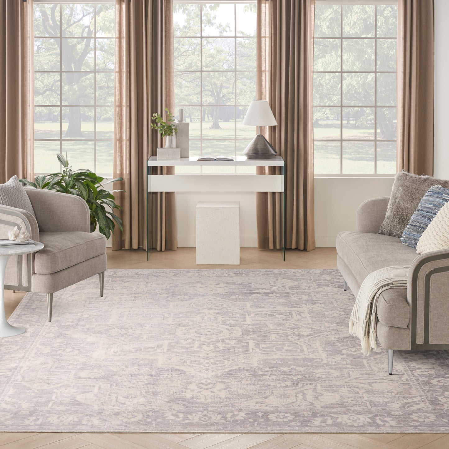 Neutral living room with beige sofas, taupe curtains, glass-top console, gray patterned rug and potted greenery.