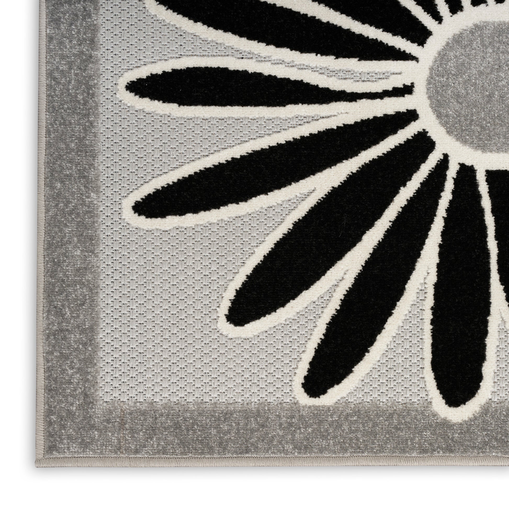 Close-up of a grey woven rug with bold black petals outlined in white forming a daisy motif and a thick border.