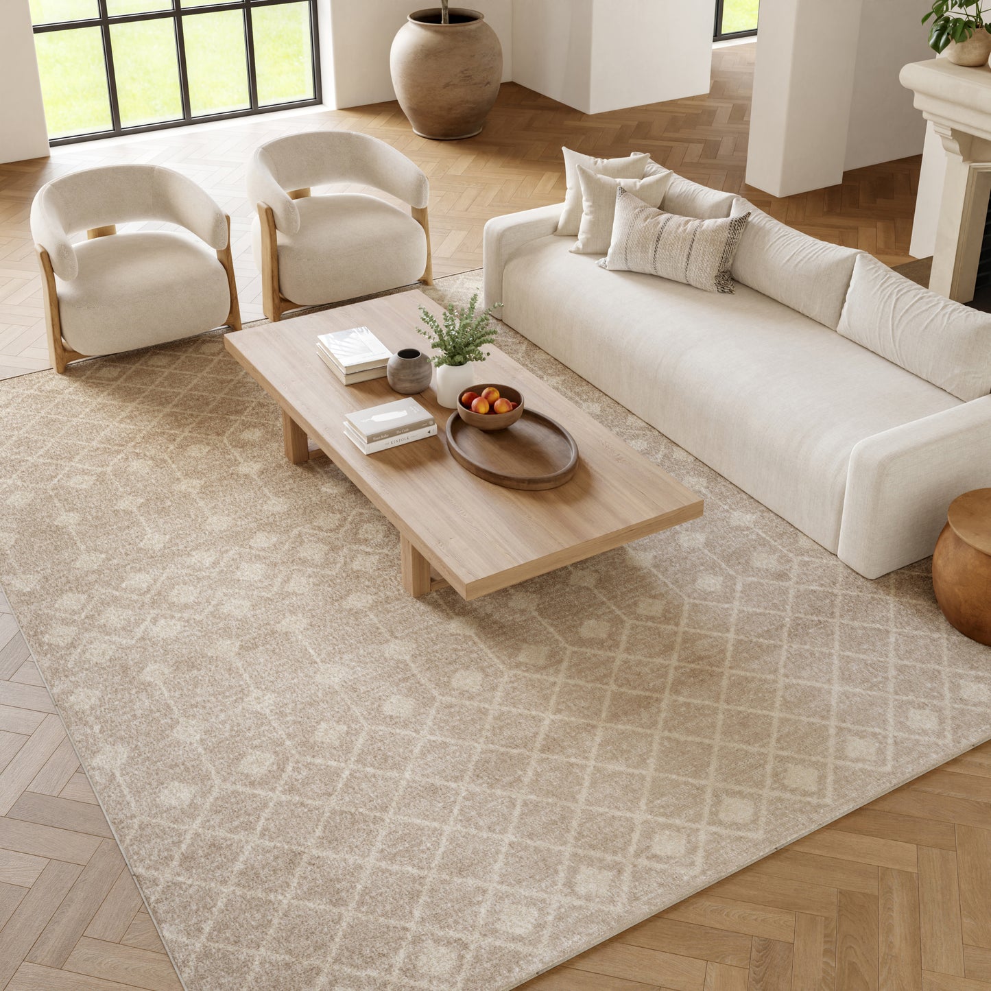Neutral living room with cream sofa & armchairs, light wood coffee table on beige patterned rug, plant & fruit bowl.