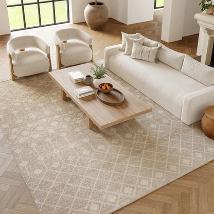 Neutral living room with cream sofa & armchairs, light wood coffee table on beige patterned rug, plant & fruit bowl.