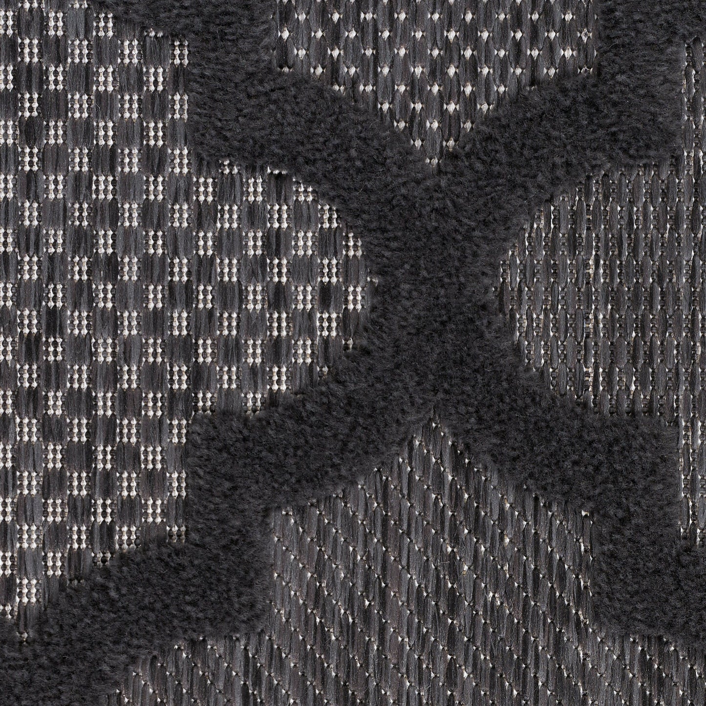 Close-up of charcoal gray woven rug with a raised black velvet X motif; bold, textured textile.