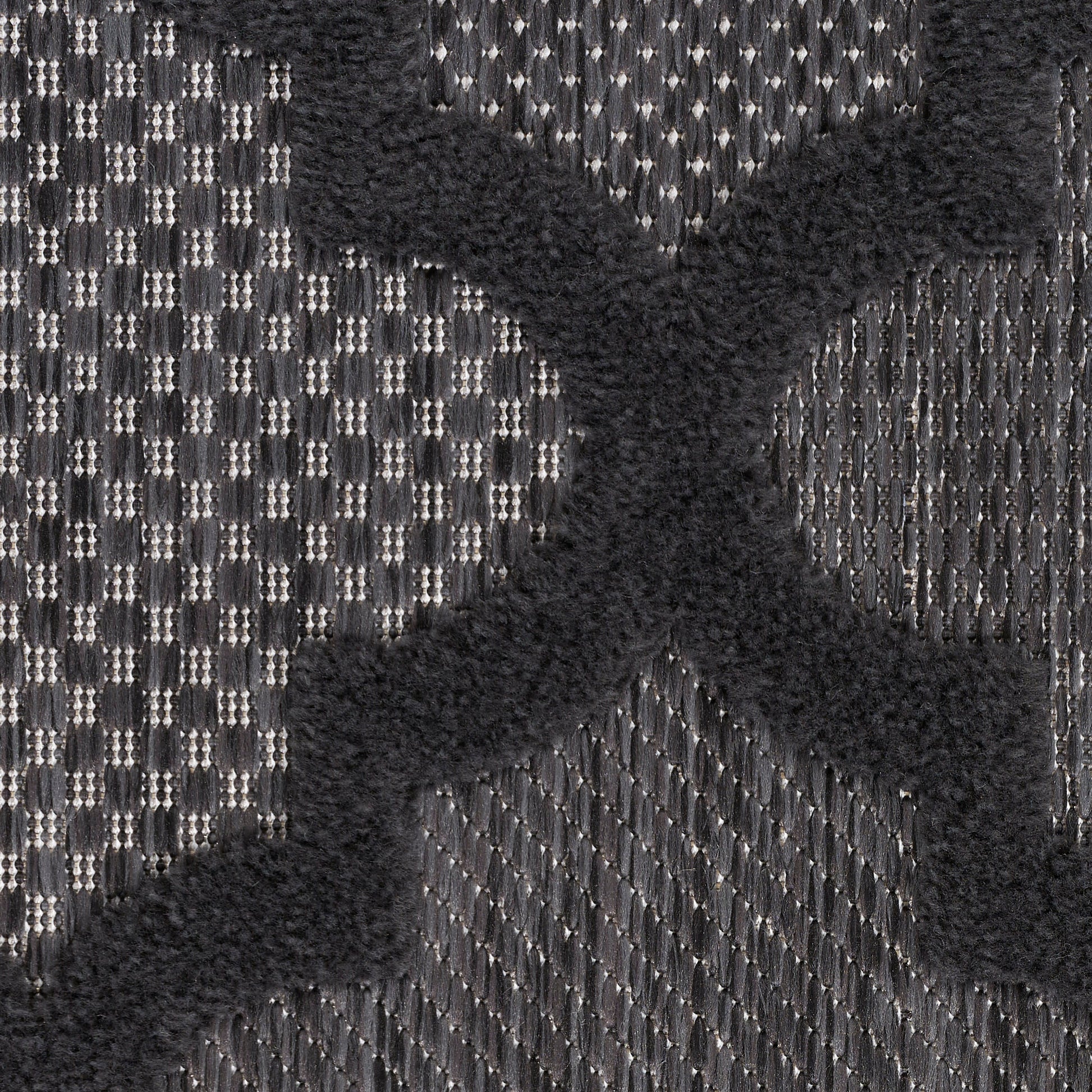 Close-up of charcoal gray woven rug with a raised black velvet X motif; bold, textured textile.