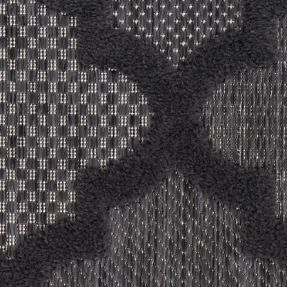 Close-up of charcoal gray woven rug with a raised black velvet X motif; bold, textured textile.