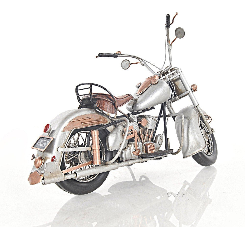 Vintage silver cruiser motorcycle with brown leather seat, chrome accents, rear rack and retro handlebars.