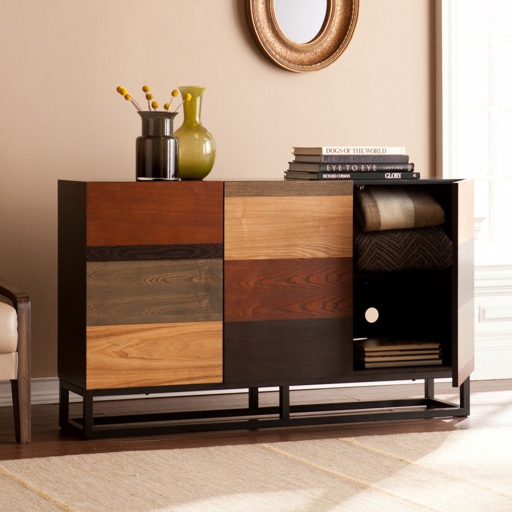 Mid-century wood sideboard with brown gray and black patchwork panels, black frame; top with vases and books, three-door cabinet.