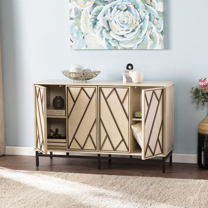 Beige wooden sideboard with geometric dark inlay and black metal legs, four cabinet doors; top decor bowls and vases on a blue wall.