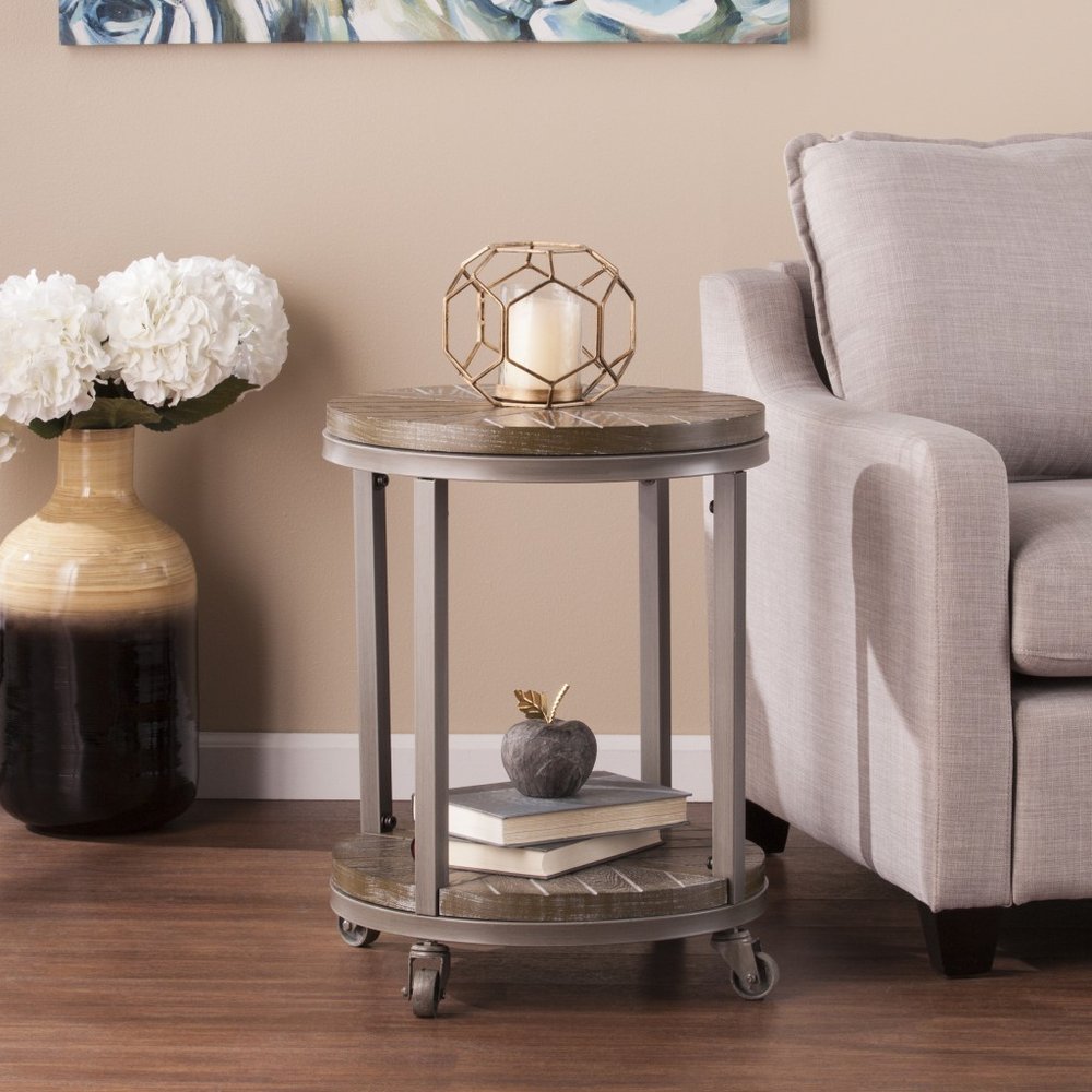 Round industrial metal side table on casters; two-tier, top candle holder, bottom books, beige living room.