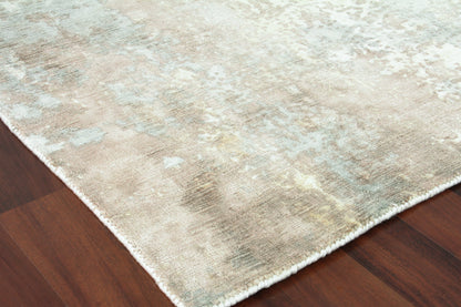 Abstract pastel area rug with beige, ivory and pale blue hues, white fringe along edges on wood floor.