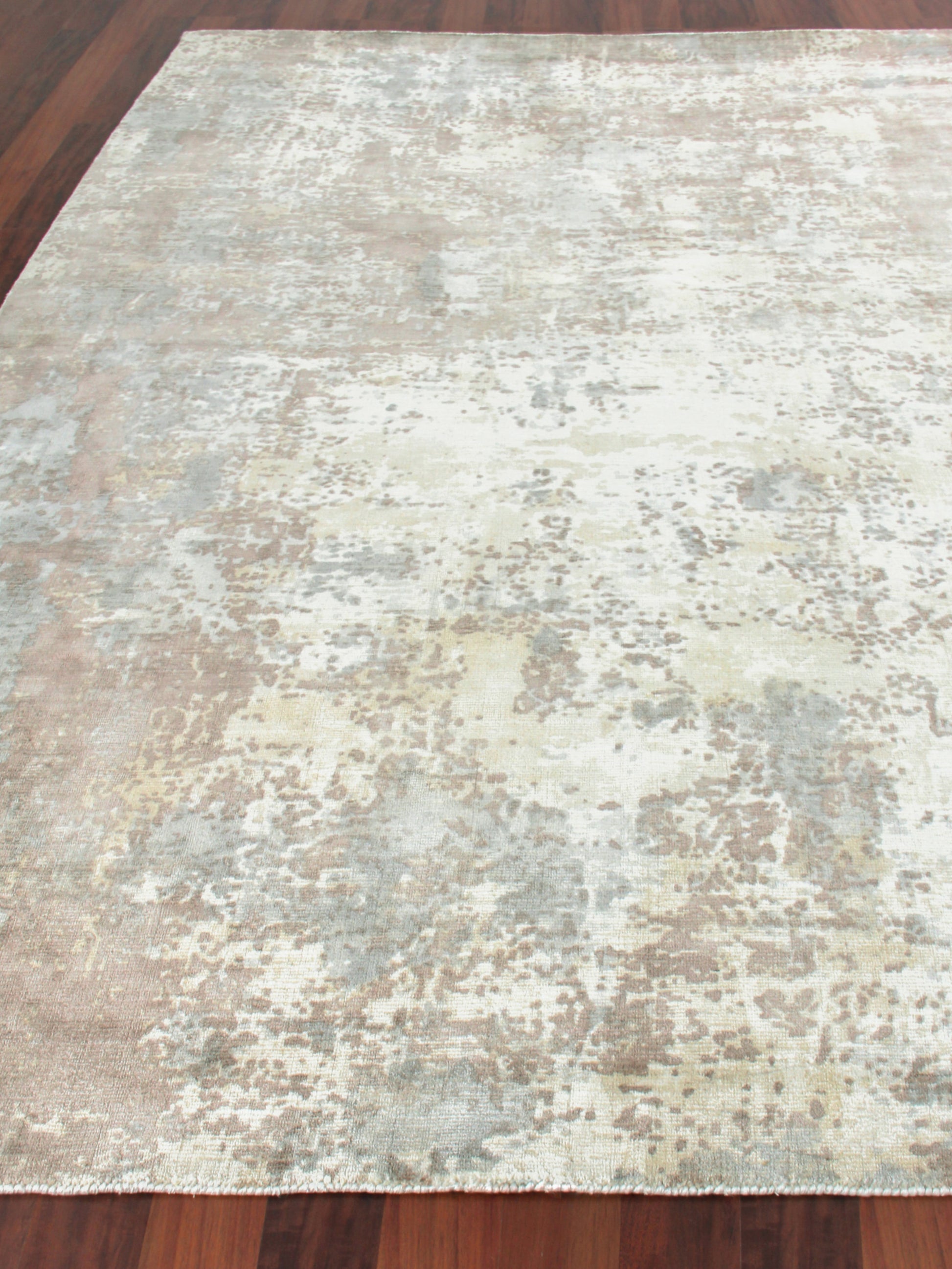 Rectangular distressed abstract area rug in cream, beige, gray and pale blue on dark hardwood floor.