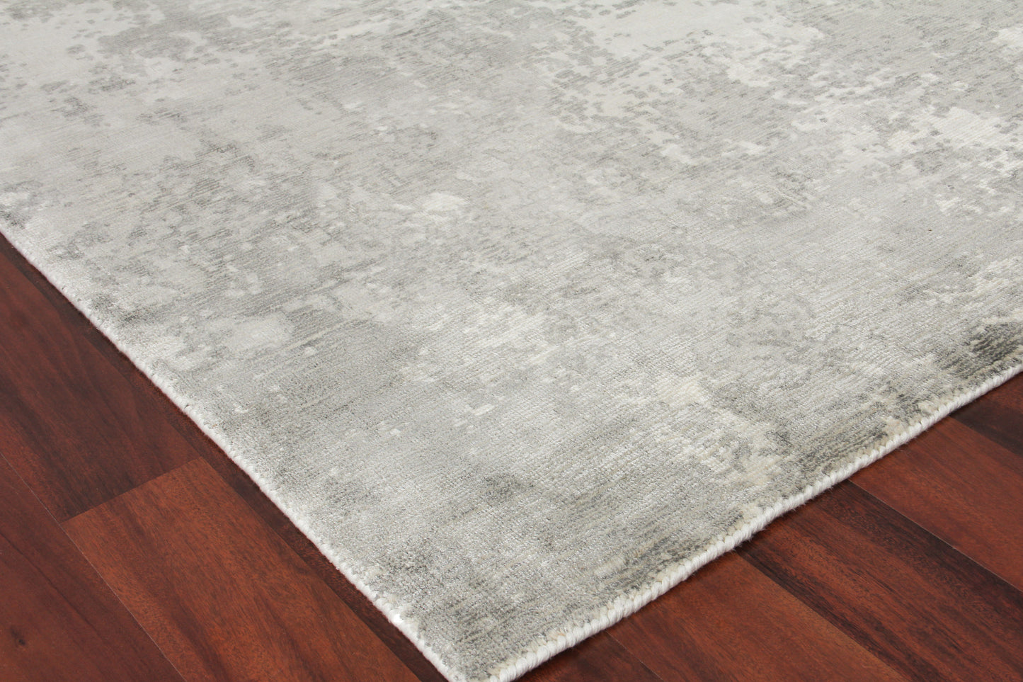 Light gray rectangular area rug with a subtle mottled texture on dark hardwood floor.