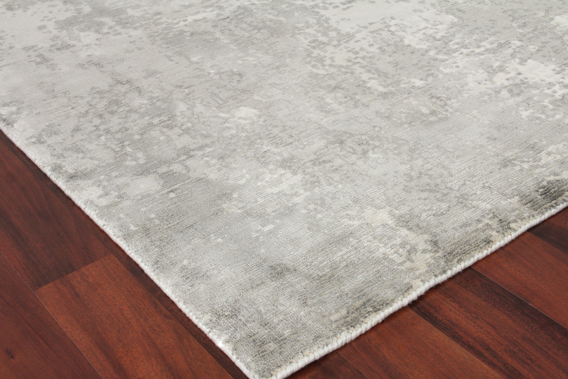 Light gray distressed area rug with plush pile on dark hardwood floor; rectangular with white fringe along edge.