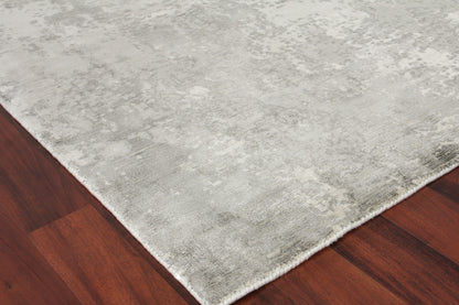Light gray distressed area rug with plush pile on dark hardwood floor; rectangular with white fringe along edge.