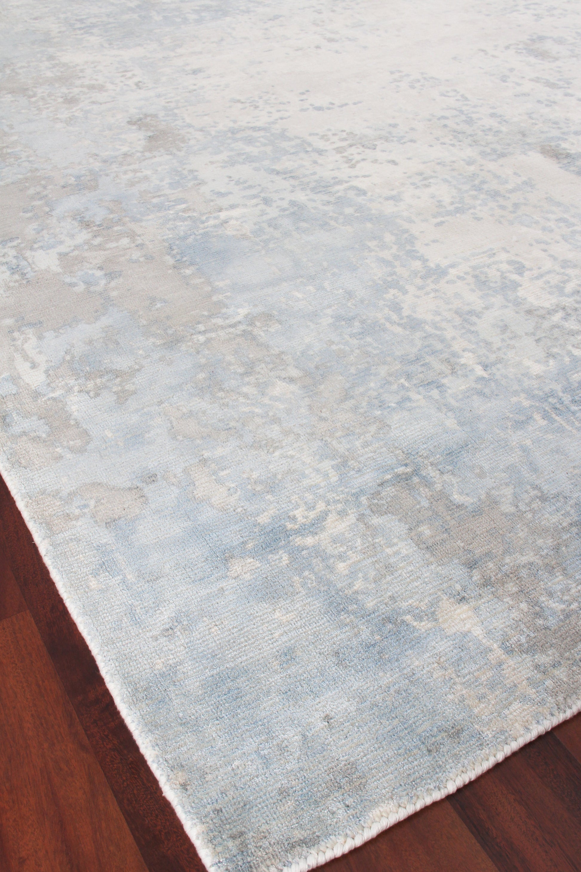 Soft blue and cream distressed-pattern area rug on dark wood floor.
