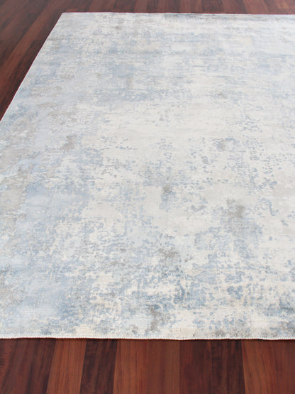 Light blue and beige distressed area rug on dark wood floor, rectangular with a subtle abstract pattern.