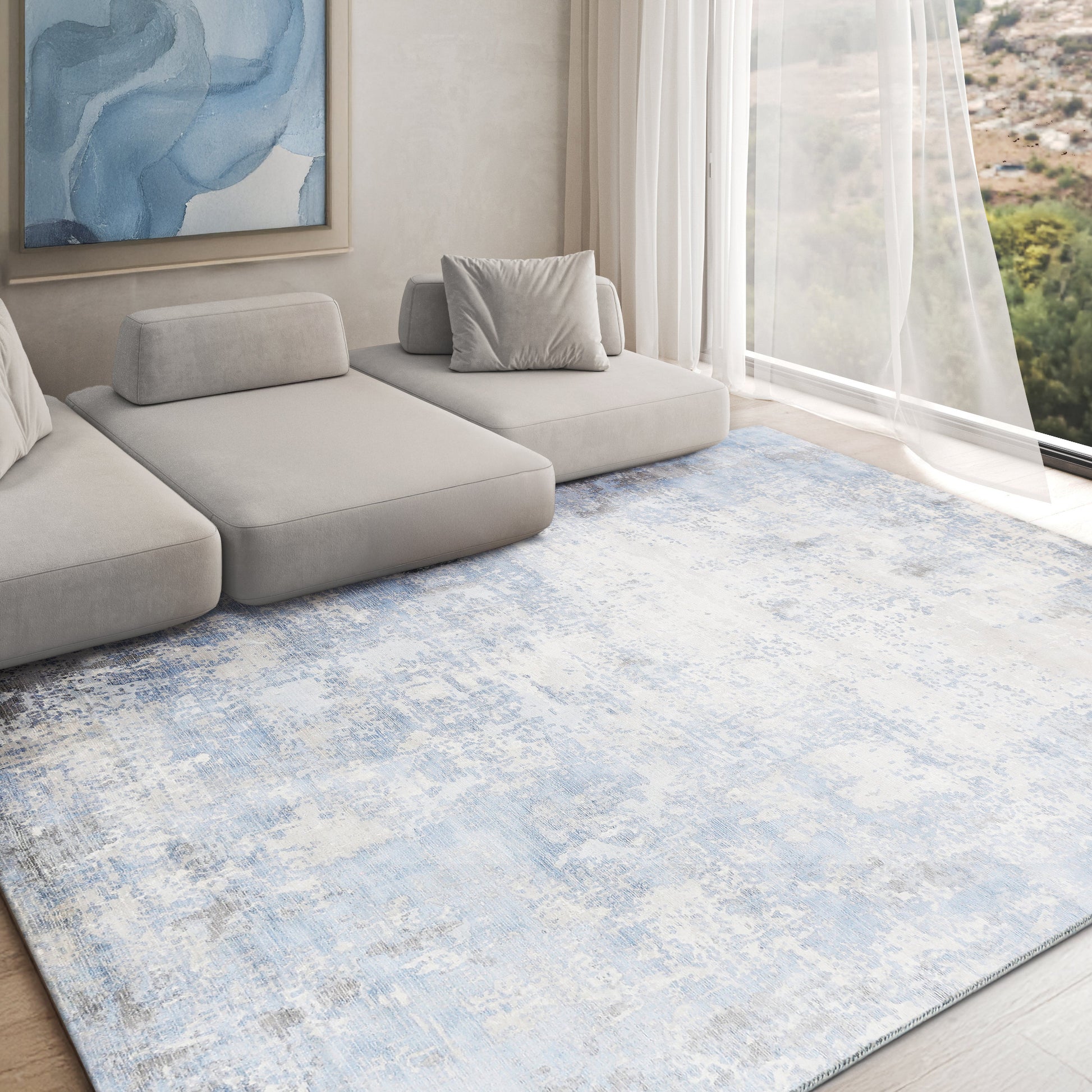 Blue abstract rug 6' x 9' in a bright living room by a large window with sheer curtains; a light gray sofa sits on the rug.
