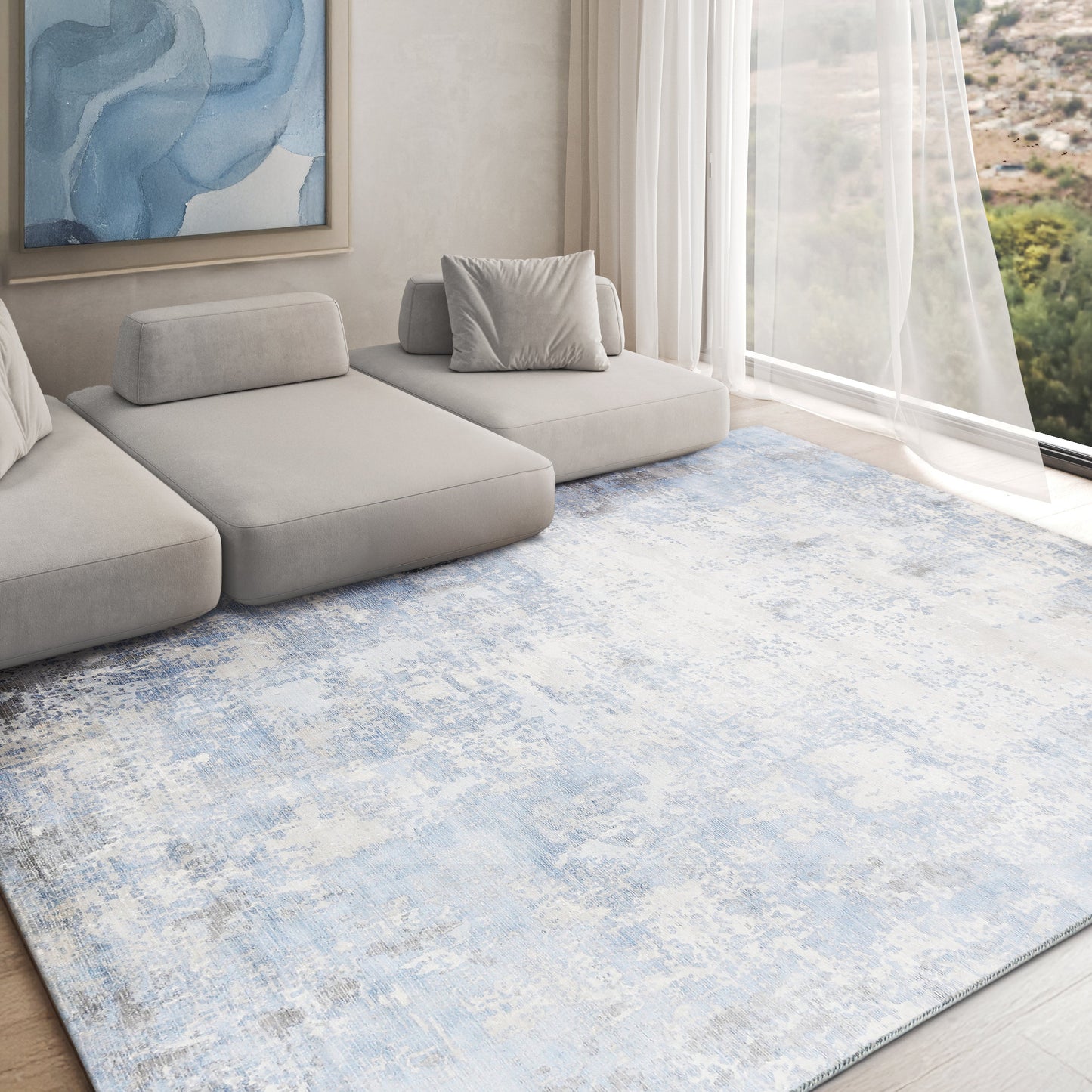 Soft blue-gray distressed area rug in a modern living room with a light gray modular sofa and sheer curtains.