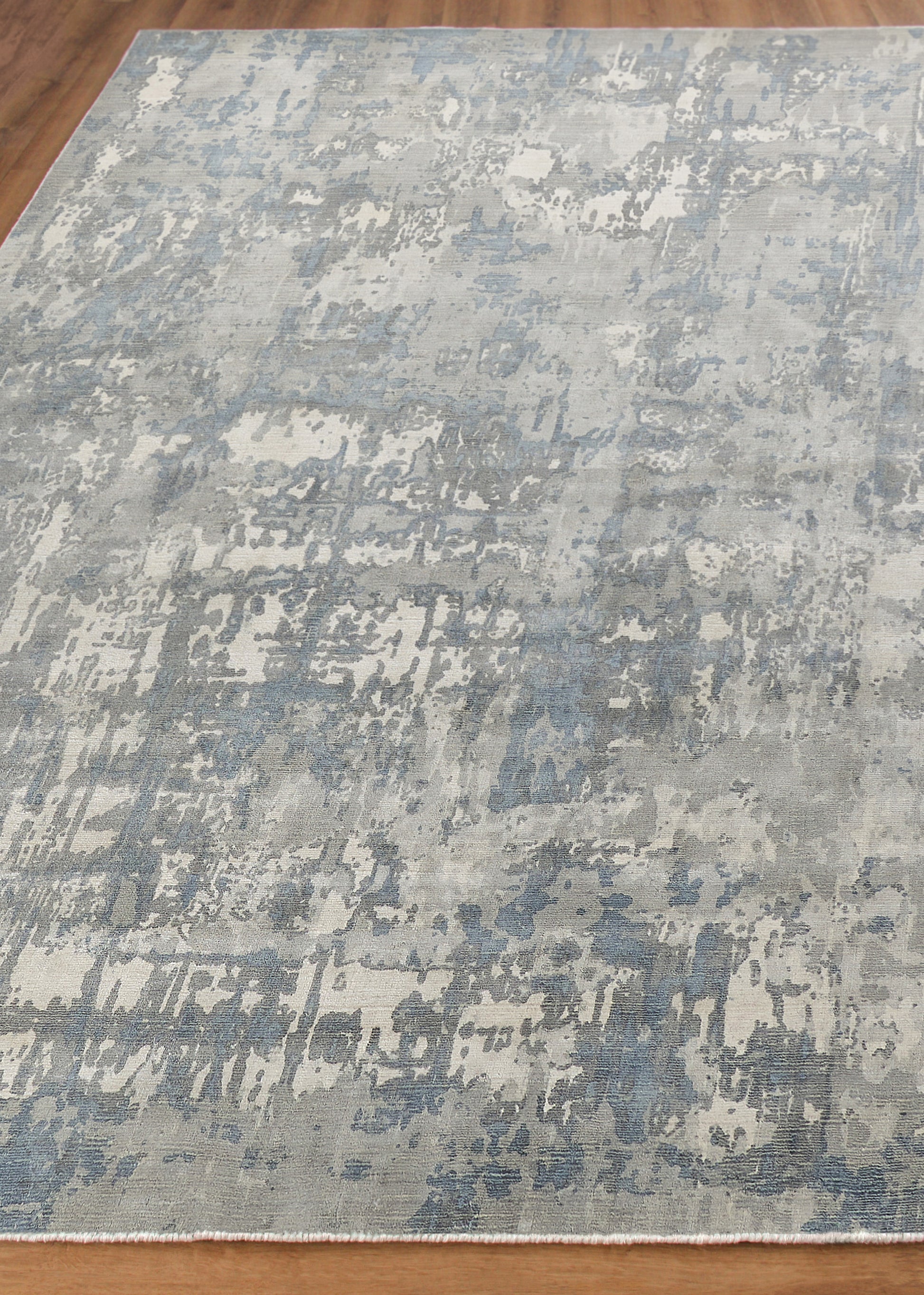 Blue-gray distressed abstract area rug with ivory highlights on wood floor.