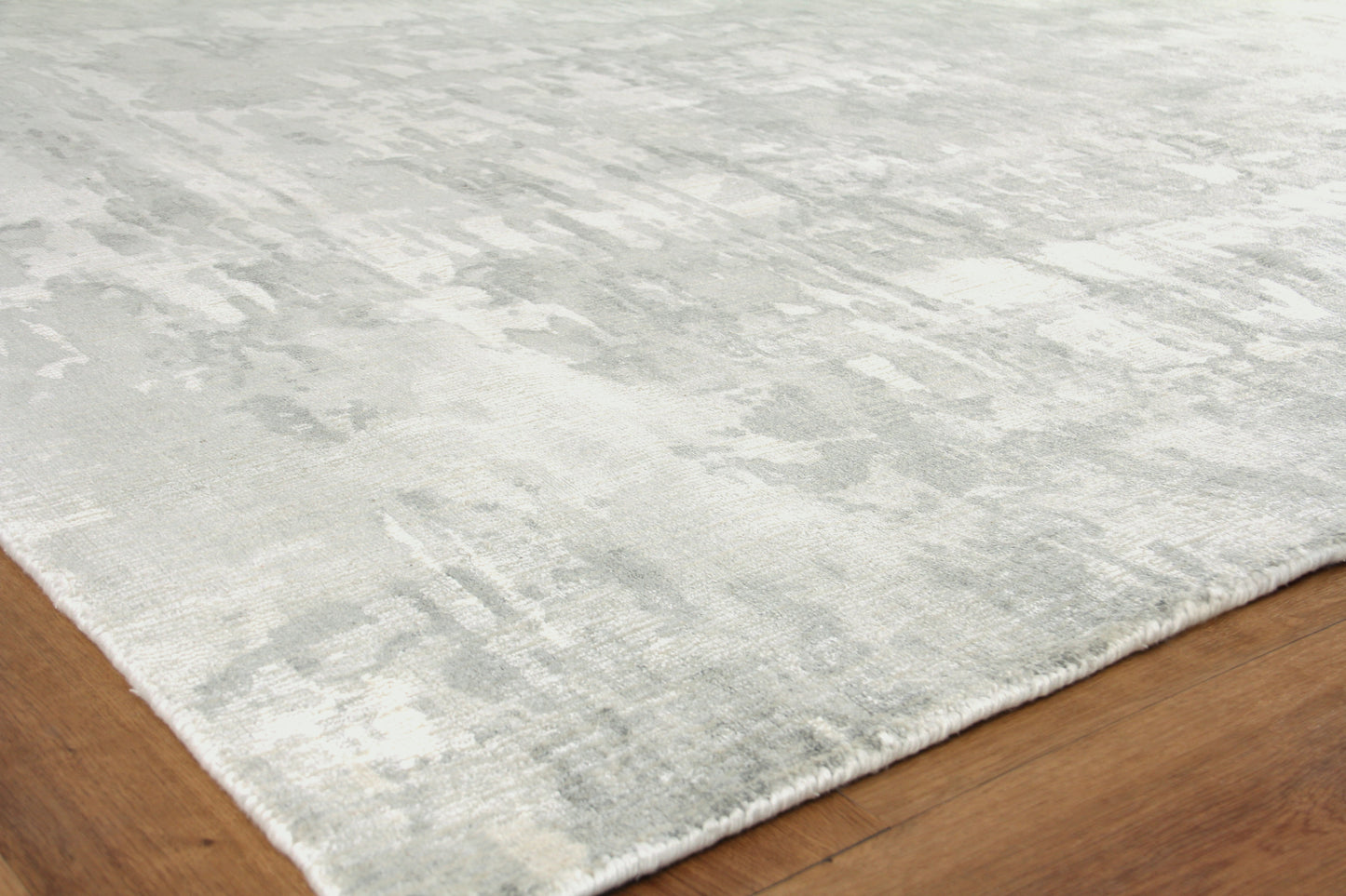 Soft gray and ivory abstract-pattern rug with fringe on a wood floor.