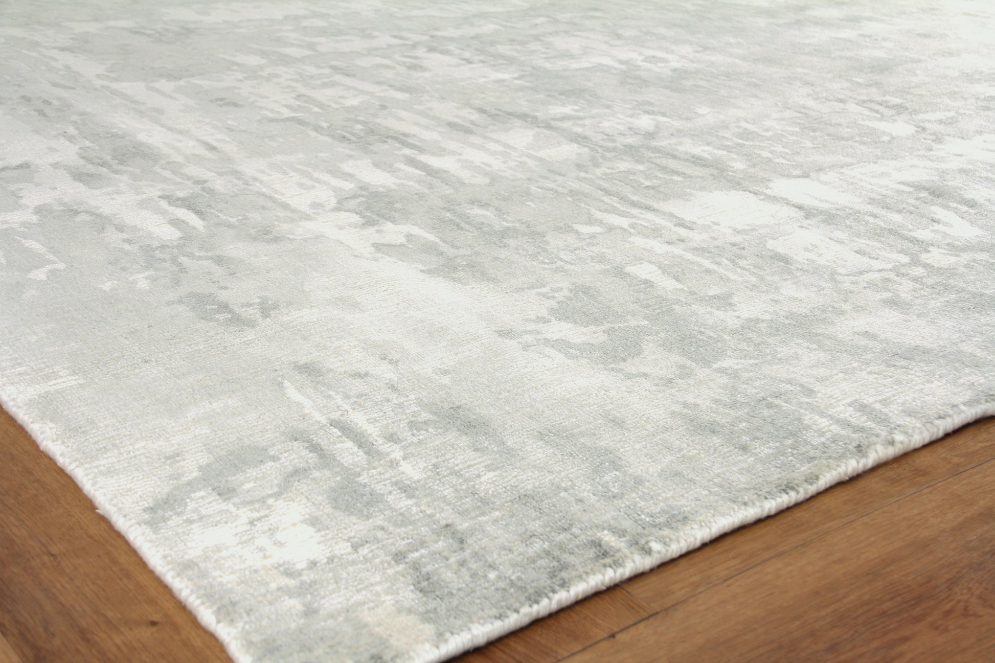 Soft gray and ivory abstract-pattern rug with fringe on a wood floor.