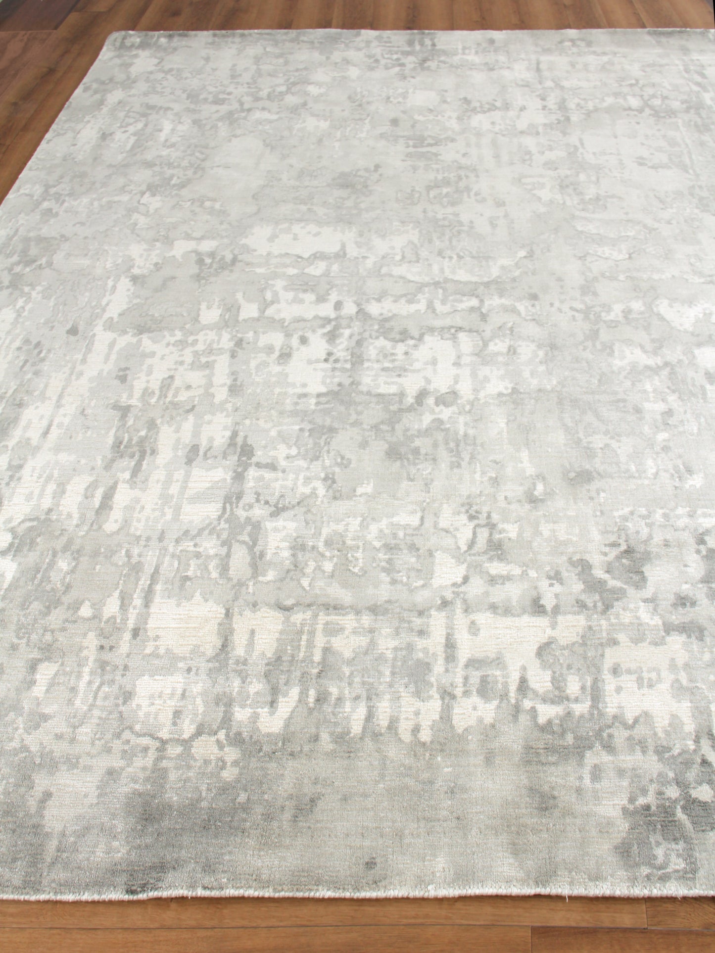 Rectangular light gray distressed abstract area rug with pale ivory tones and soft pile on wood floor.