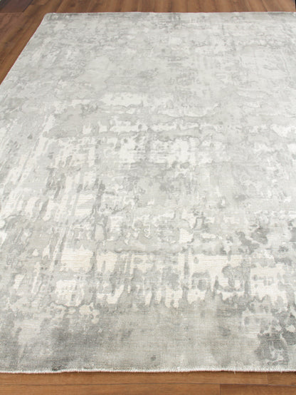 Rectangular light gray distressed abstract area rug with pale ivory tones and soft pile on wood floor.