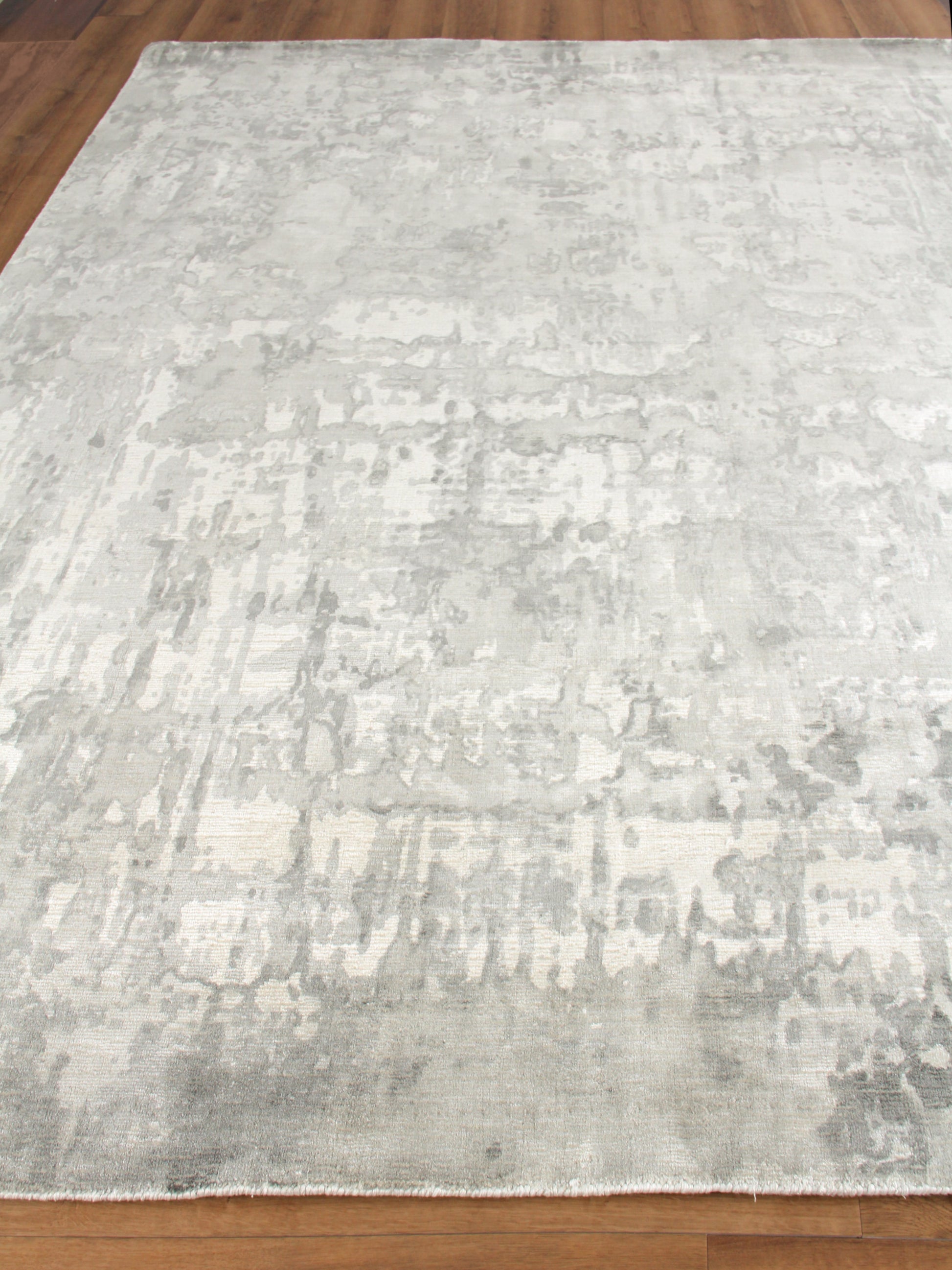 Rectangular light gray and ivory distressed abstract area rug with subtle pattern on hardwood floor.