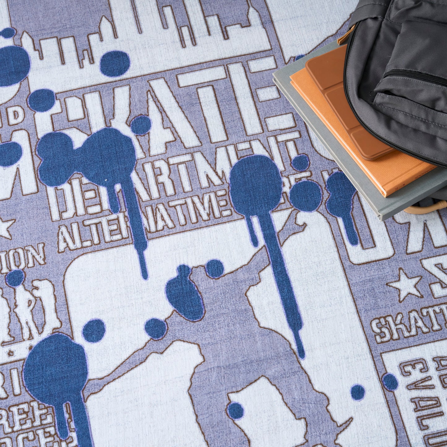Blue graffiti rug with silhouette figure, paint drips and bold text; backpack and notebooks on edge.